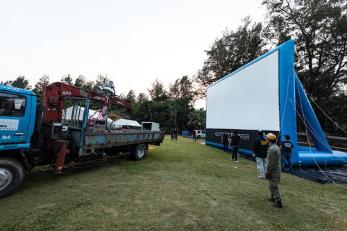 青空の芝生でアウトドアシアターの大型スクリーンを設営中