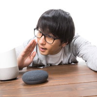 机の黒いスマートスピーカーに話しかける男性の写真