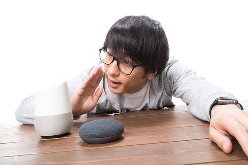 机の黒いスマートスピーカーに話しかける男性