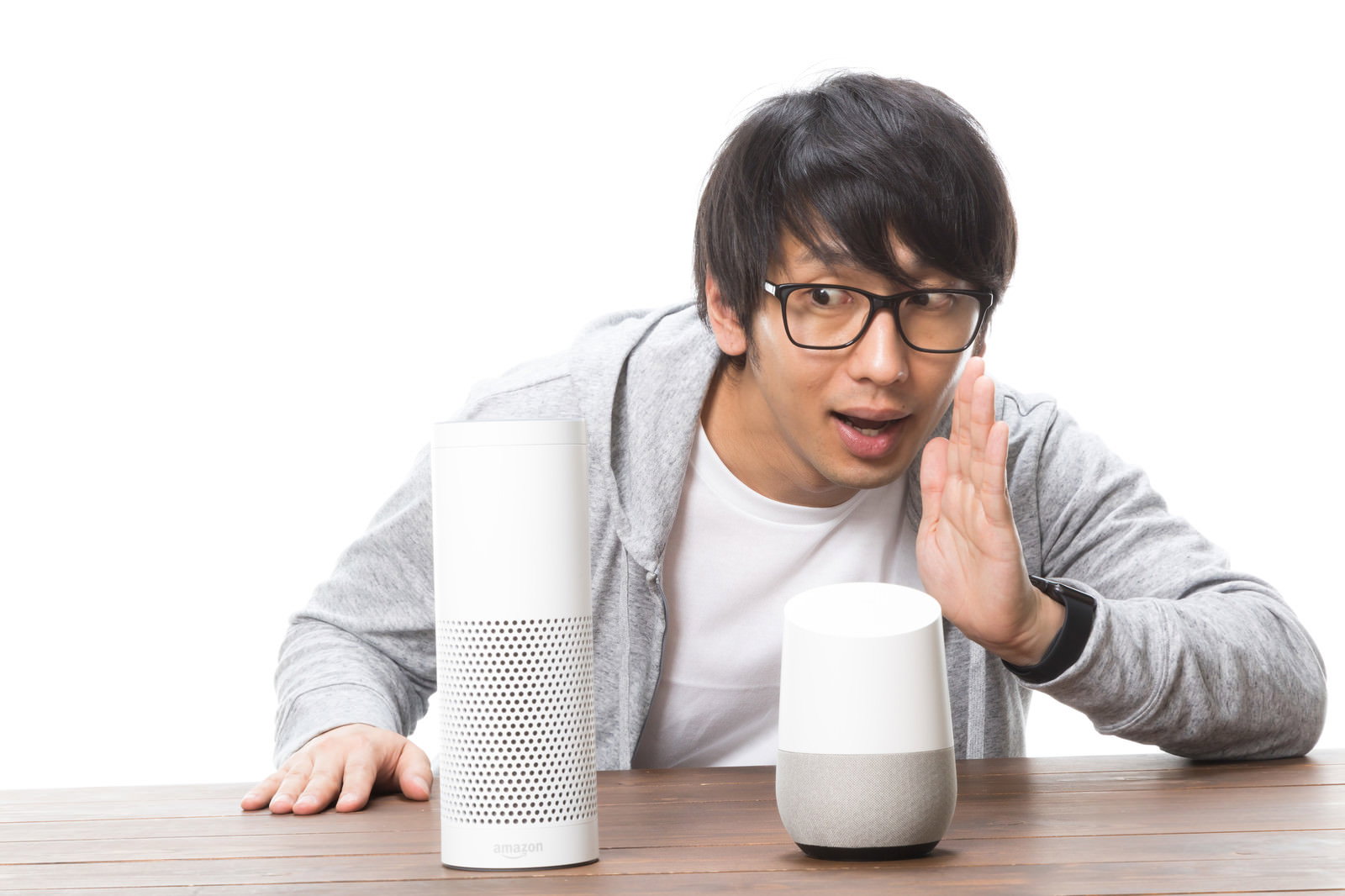 眼鏡をかけた男性がテーブルの白いスマートスピーカーに話しかけている［モデル：大川竜弥］