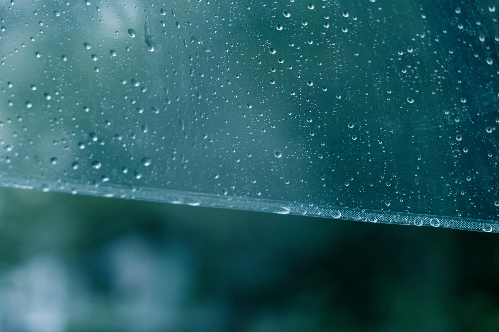 透明なビニール傘の表面に無数の雨粒が付着している様子