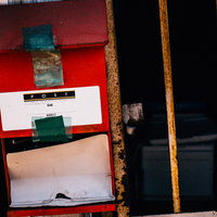 無人の廃屋に残された赤い郵便受けと玄関ドアの写真