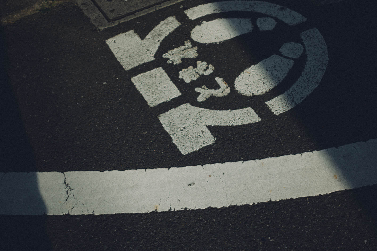 歩道に白いペイントで描かれたとまれの文字と矢印標示