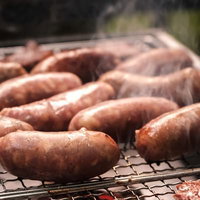 炭火で網焼きしているソーセージ、複数本が香ばしく焼き色がついた様子の写真