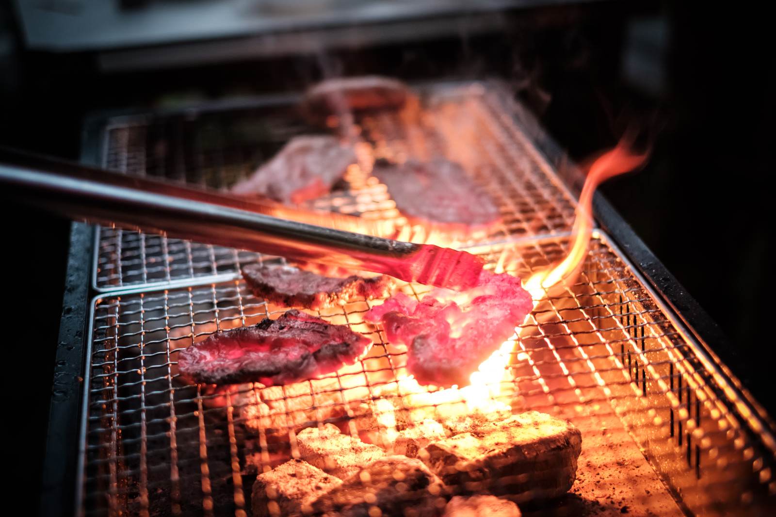 網の上で焼肉を焼いている際に肉の脂が炭火に落ちて炎が上がっている様子