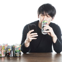 スマホを見ながらストロングゼロを飲む男性の写真