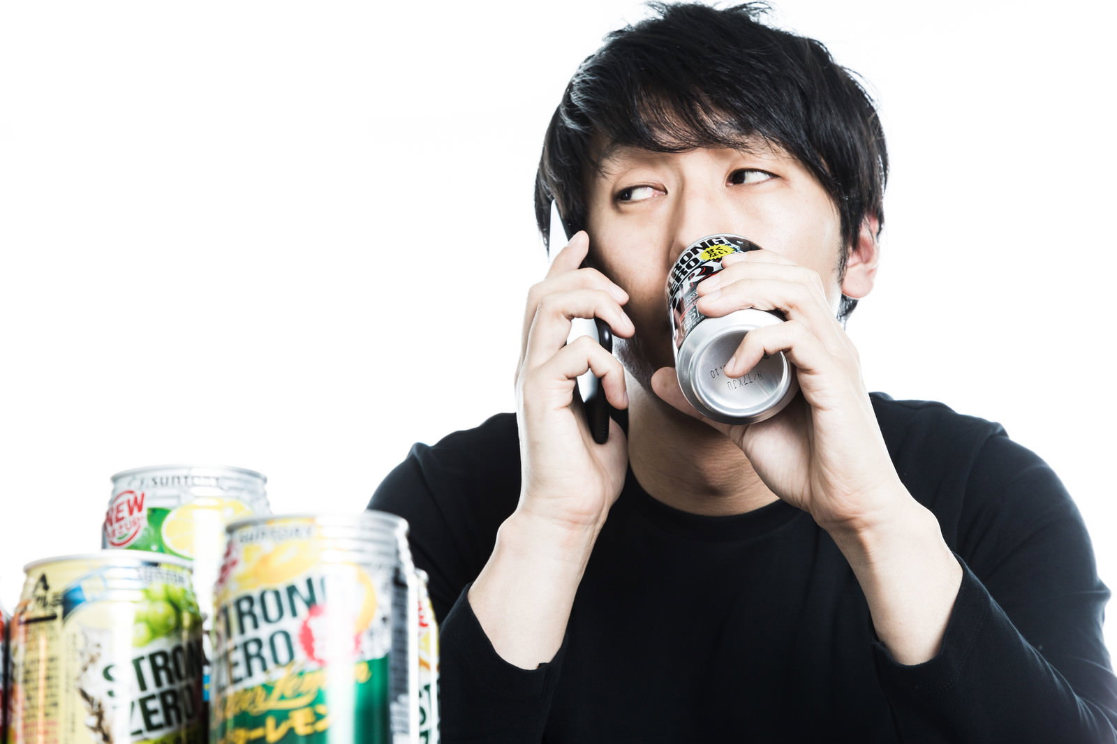 昼間から缶チューハイを飲みながらスマートフォンで通話する黒いTシャツの男性［モデル：大川竜弥］