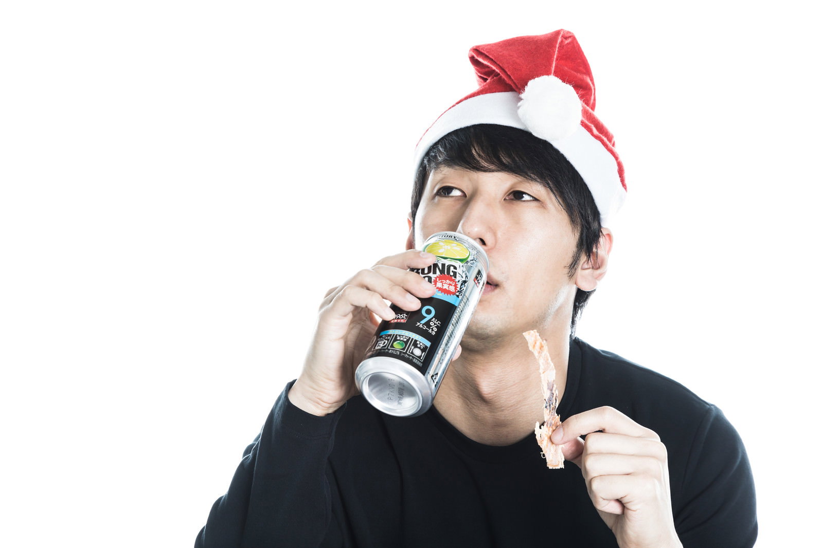 サンタ帽をかぶり、ストロングゼロを飲みながらあたりめを食べている黒いTシャツの男性［モデル：大川竜弥］