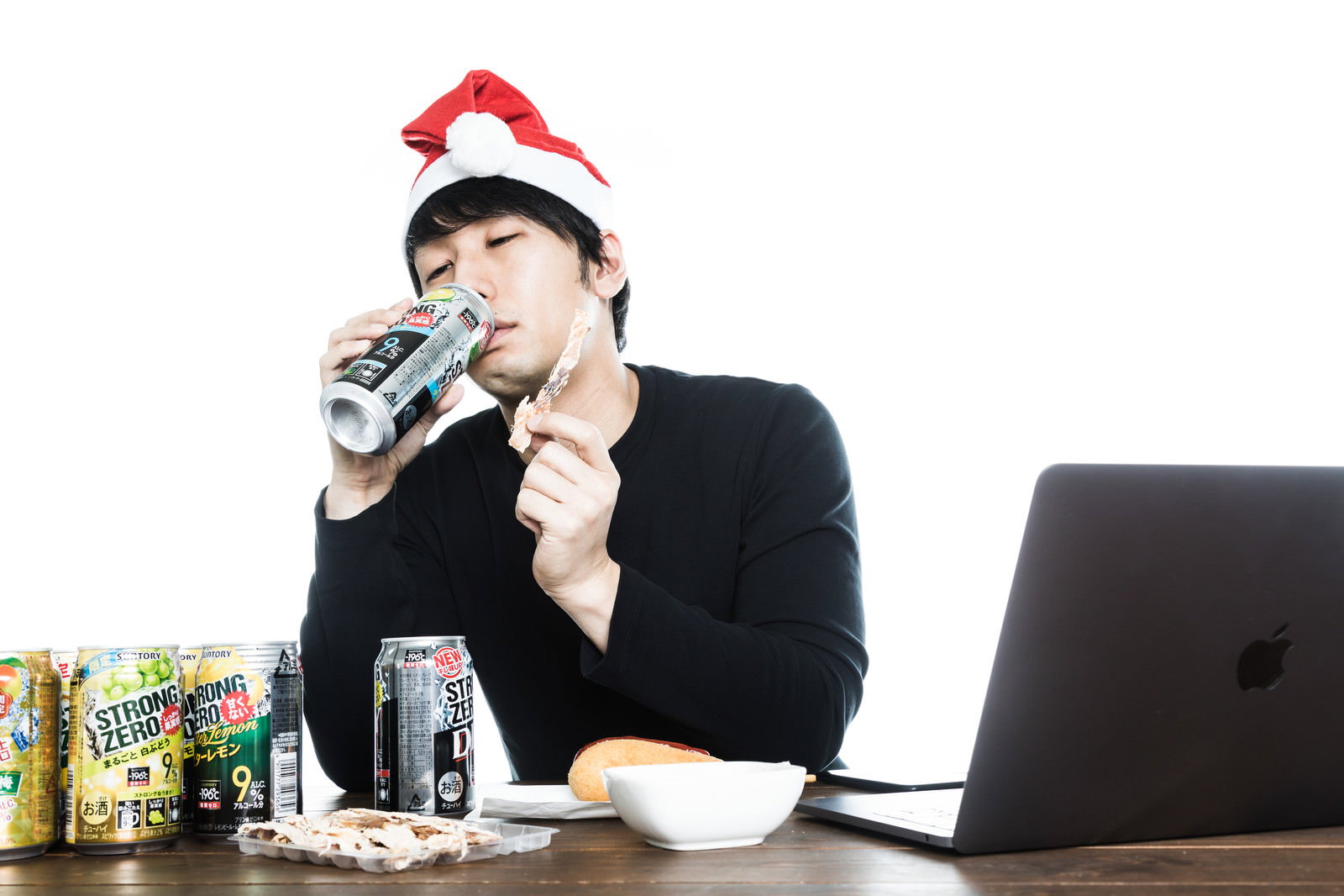 デスクでサンタ帽をかぶりながら缶チューハイを飲む黒スーツの男性［モデル：大川竜弥］