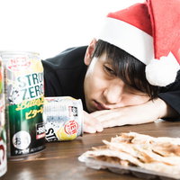 目覚めの一杯も缶チューハイ、サンタ帽姿で机に寝込む男性の写真