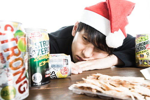目覚めの一杯も缶チューハイ、サンタ帽姿で机に寝込む男性