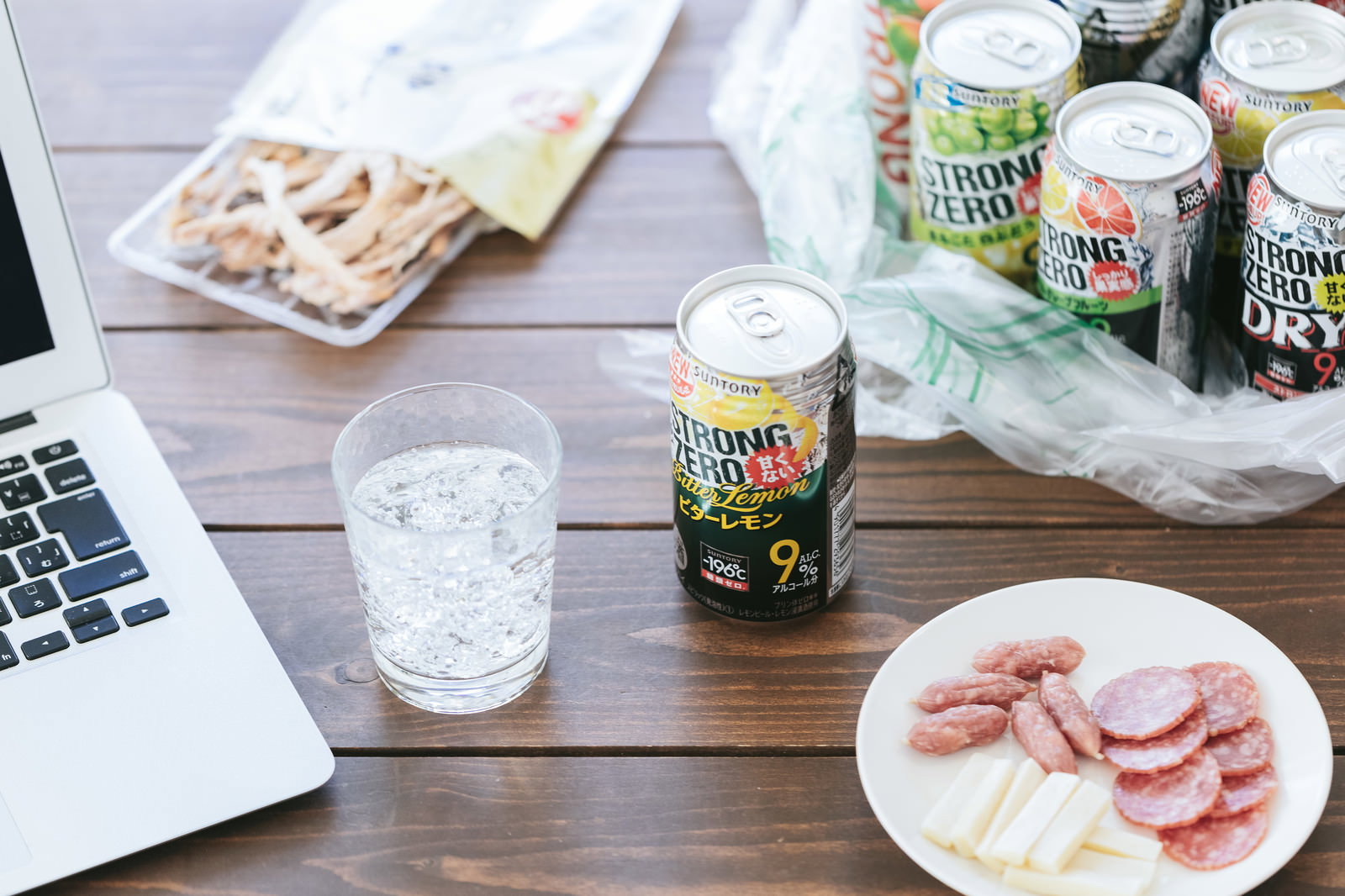 デスクの上に並ぶ缶チューハイとおつまみとノートパソコン