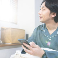 朝日が差し込む中、スマホのアラームが鳴る前に目覚めた男性の写真