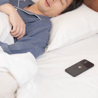 枕元に置かれたスマートフォンと熟睡する男性の写真