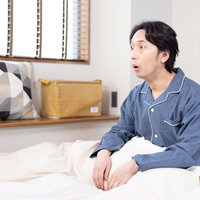 寝室で久々の快眠に驚く男性の写真