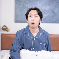 朝目覚めて寝坊に驚く男性の写真