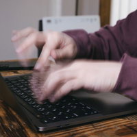ノートパソコンのキーボードで高速タイピングする男性の写真