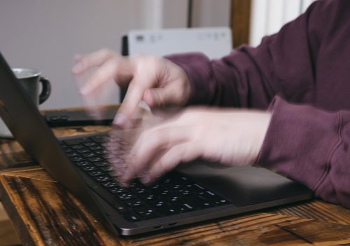 ノートパソコンのキーボードで高速タイピングする男性