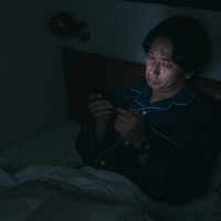 眠れなくてベッドでスマホ動画を見てしまう男性の写真