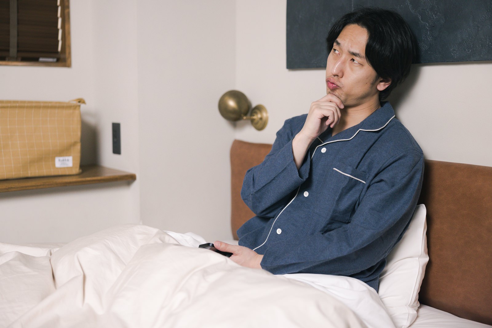 ベッドでスマホを持ち考える男性［モデル：大川竜弥］