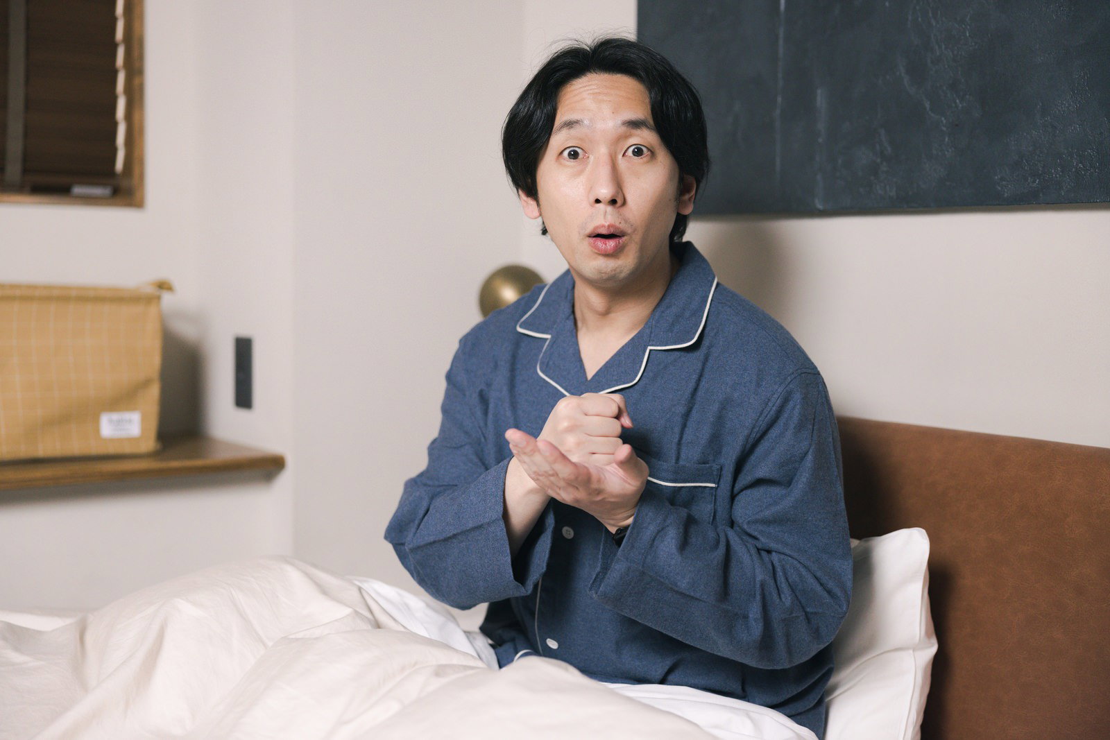 ベッドで驚いた顔をするパジャマ姿の男性［モデル：大川竜弥］