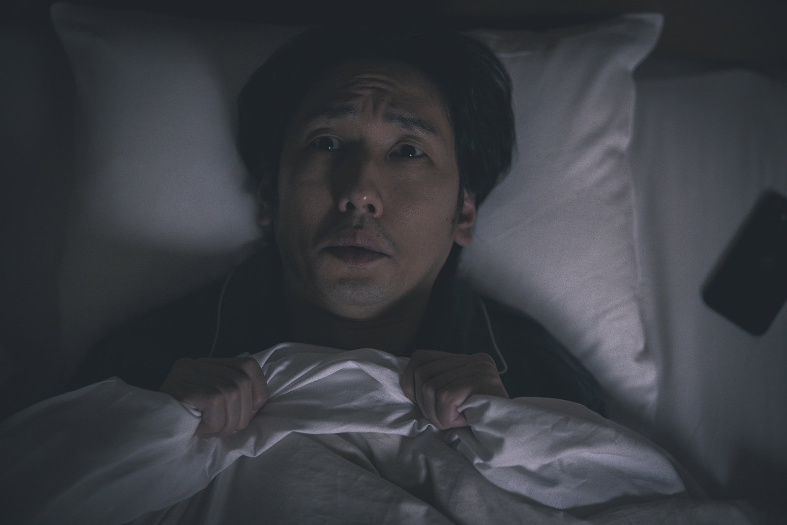 ベッドで横になりながら目を開けて眠れずにいる男性［モデル：大川竜弥］