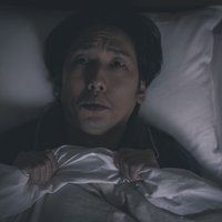 寝なきゃダメだ、寝なきゃダメだと頭を抱える不眠の男性の写真