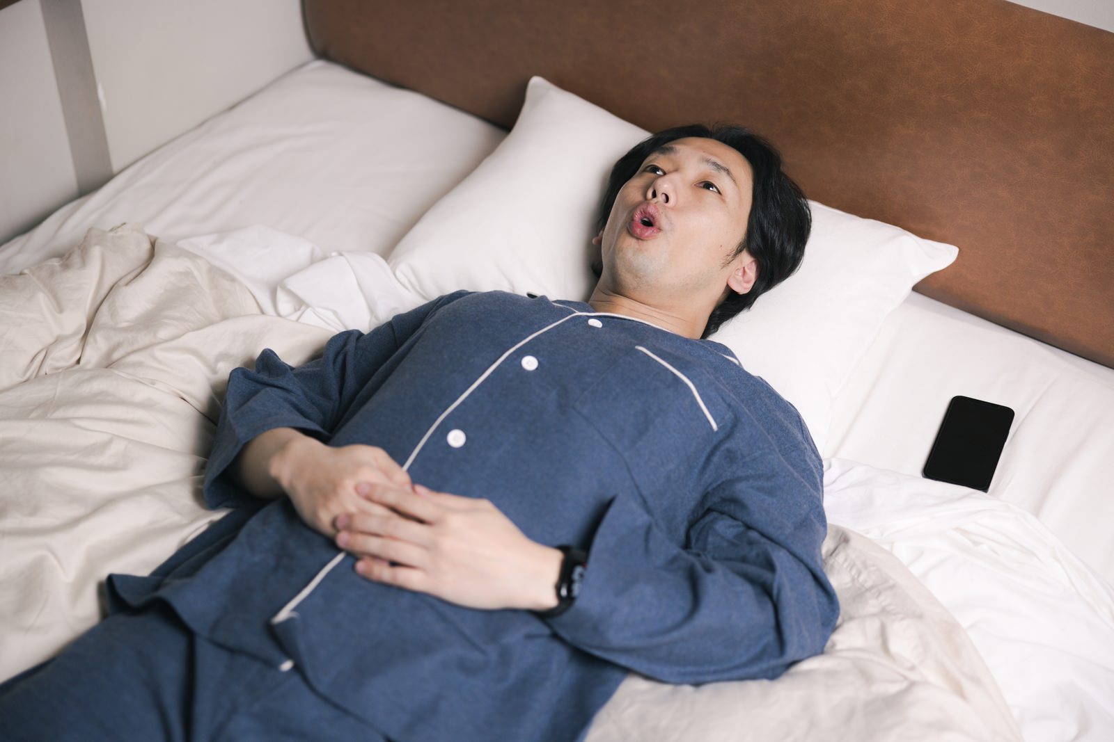 紺色のパジャマを着た男性がベッドで仰向けに横になっている［モデル：大川竜弥］