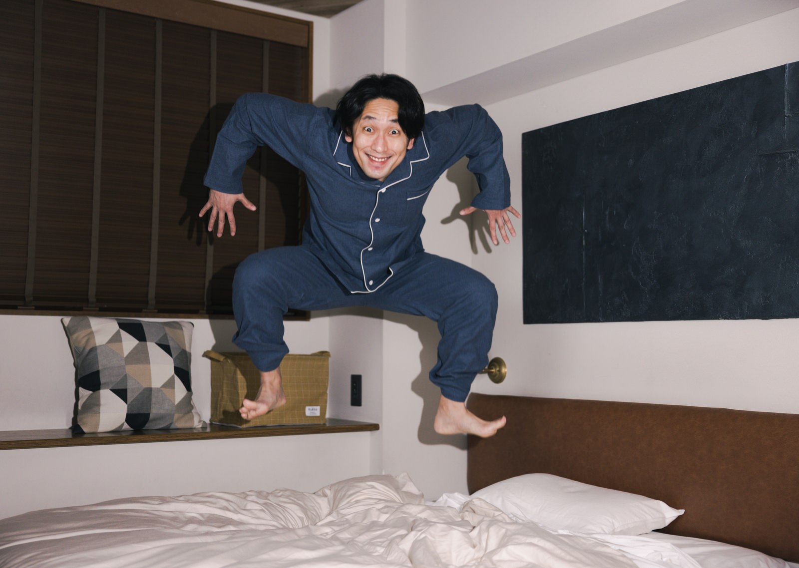 ベッドの上で飛び跳ねるハイテンションな男性［モデル：大川竜弥］