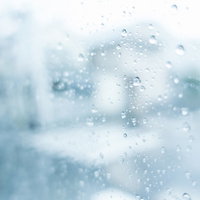 窓ガラスに付着した雨粒と曇り空の写真