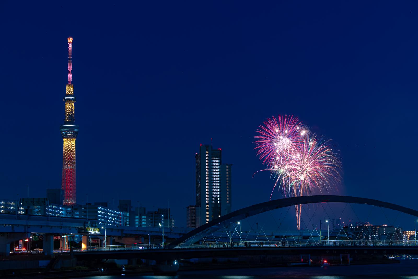 夜間にスカイツリーと花火が映る隅田川の橋からの景観