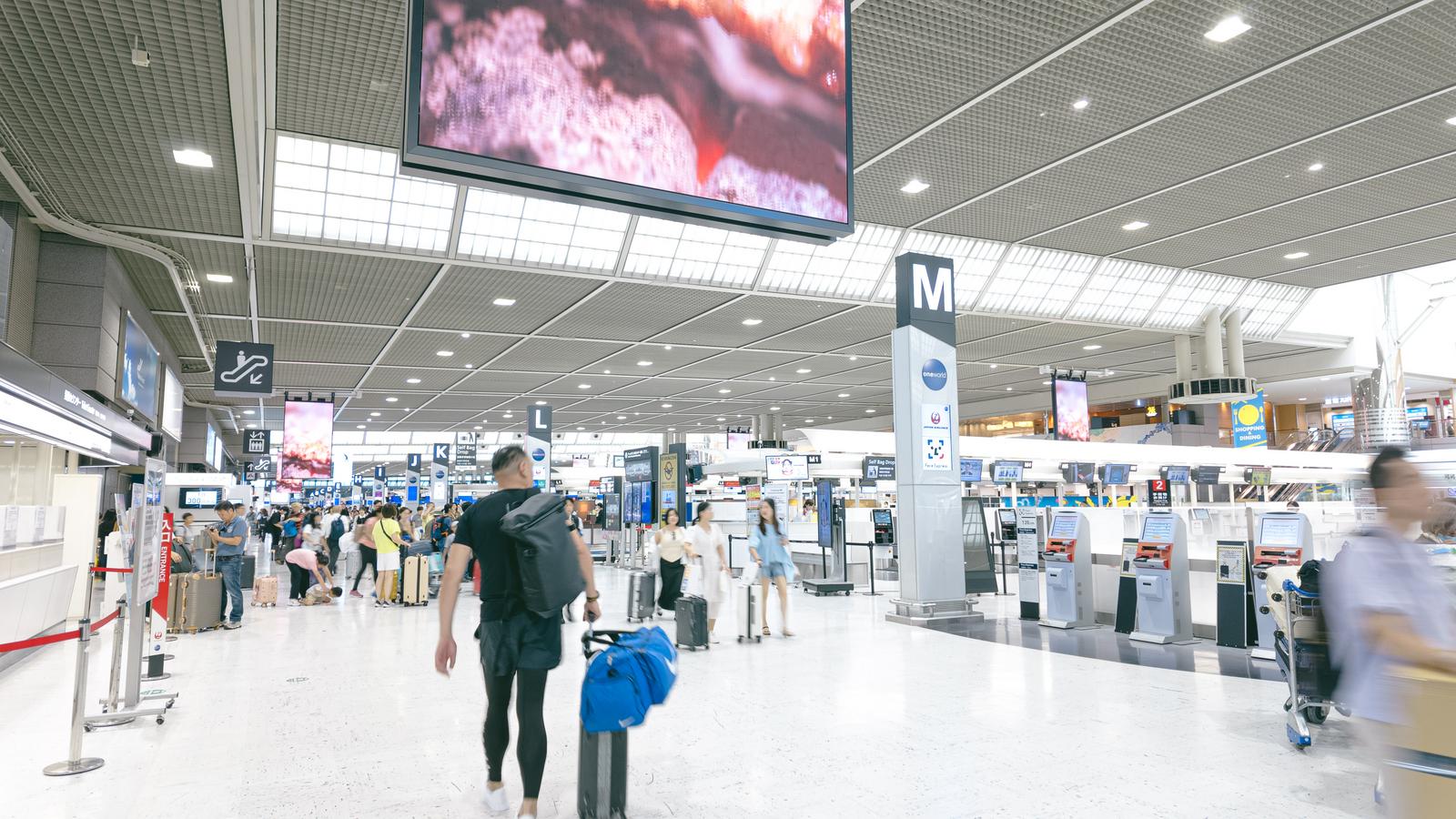 成田空港国際ターミナルの出発ロビーで旅行客がスーツケースを持ちながら移動している風景