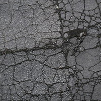 ひび割れたアスファルトと溝に詰まる土のテクスチャーの写真