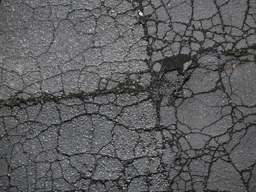 ひび割れたアスファルトと溝に詰まる土のテクスチャー