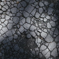 ひび割れたアスファルトに残る影と細かなテクスチャーの写真