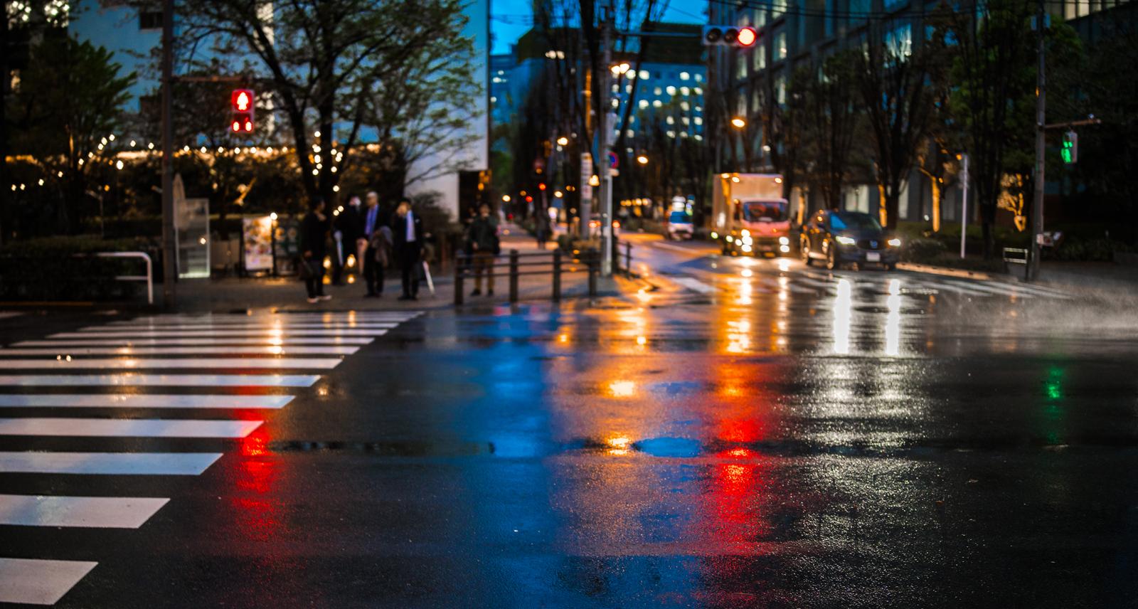 Low-angle photograph of traffic signal and streetlight reflections on a wet crosswalk at dusk after rain