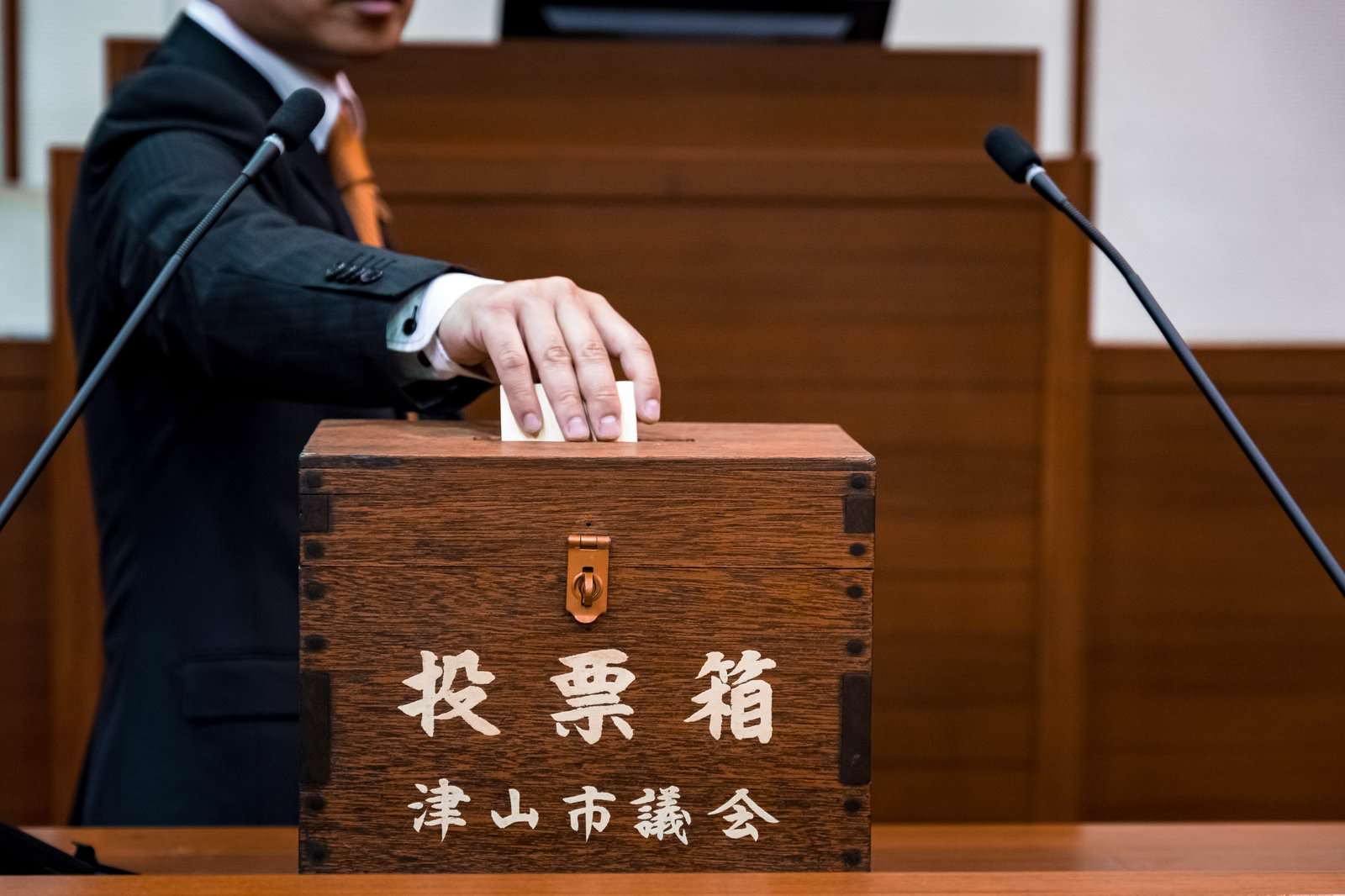 津山市議会の投票箱に投票用紙を入れる議員の手