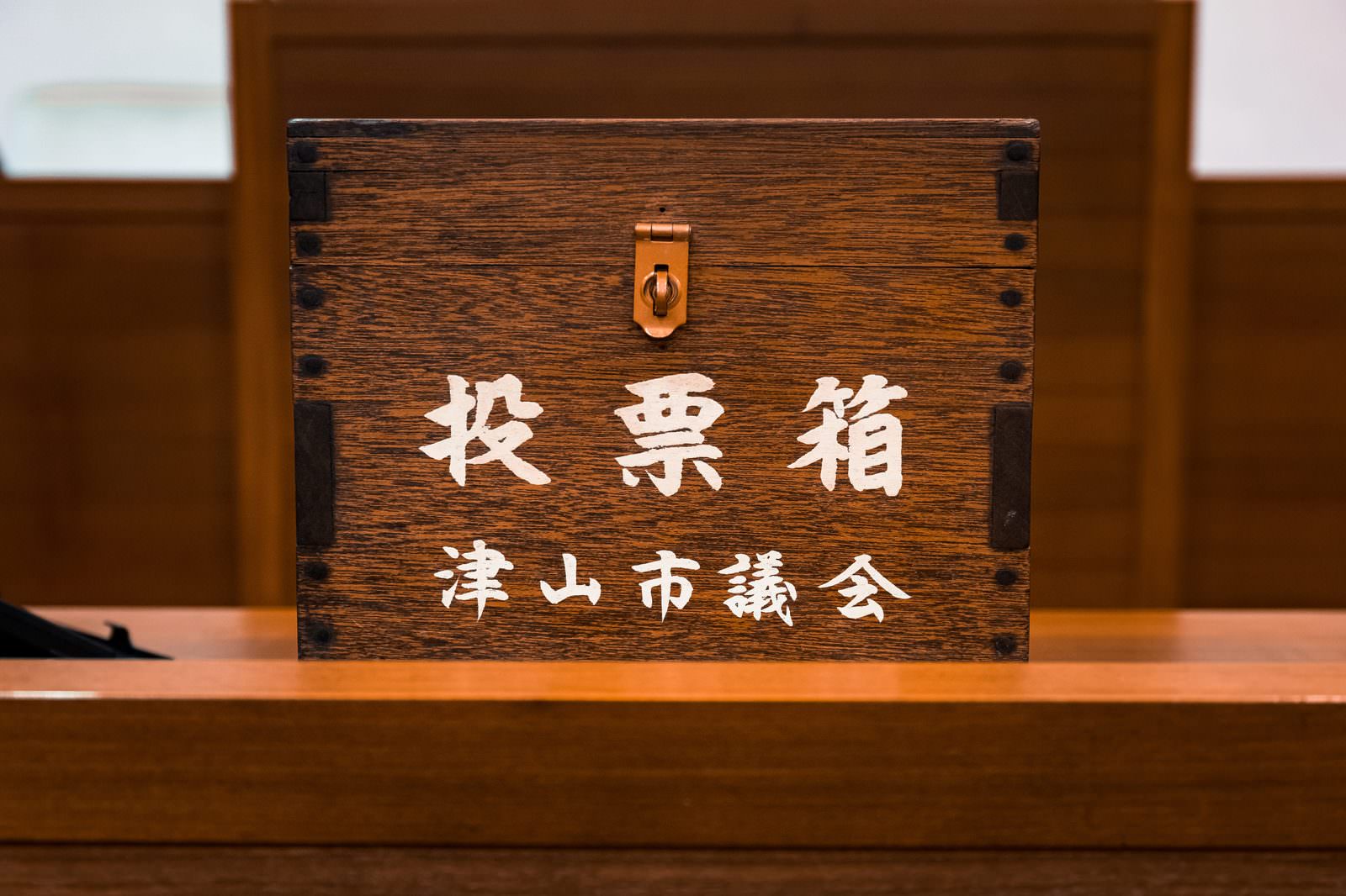津山市議会の投票箱。濃い茶色い木製で金色の錠前が付き、白い文字で投票箱と市議会の名前が刻印されている
