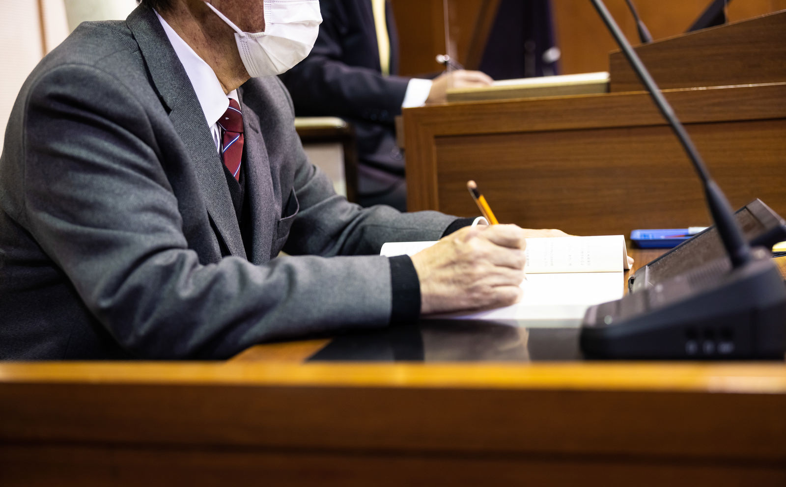 議場で書類にメモを取るマスク姿の男性議員