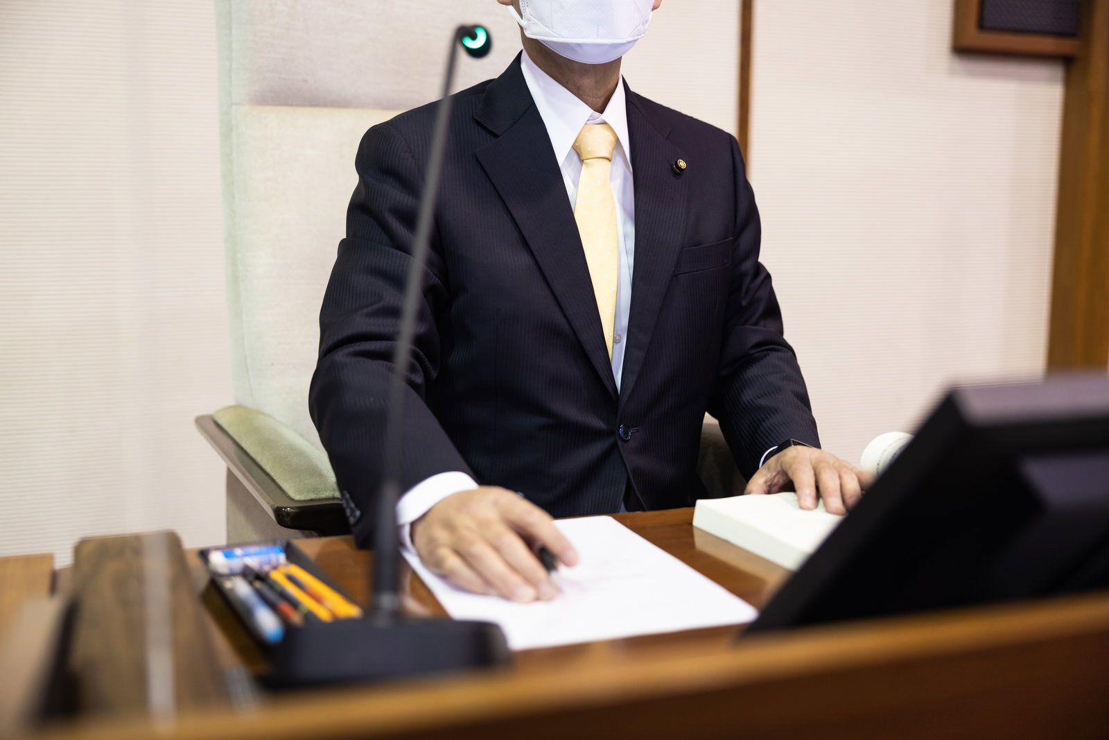 議場の議長席で書類確認をする紺色の背広姿の男性議員