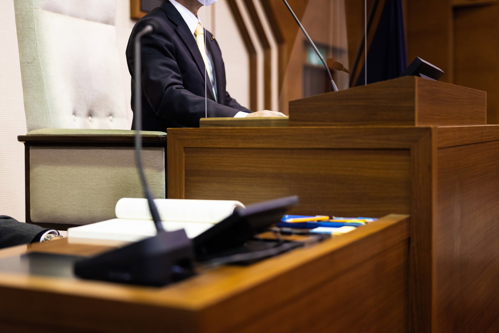 議場の議長席で書類を確認する紺色スーツの議長