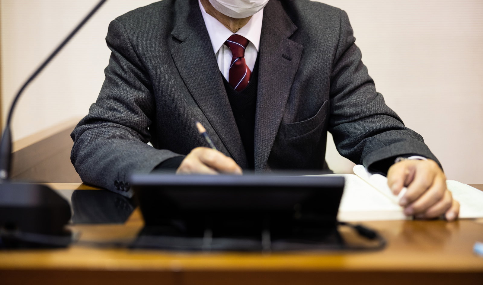 議場で鉛筆を逆さまに持ってメモを取ろうとしている男性議員