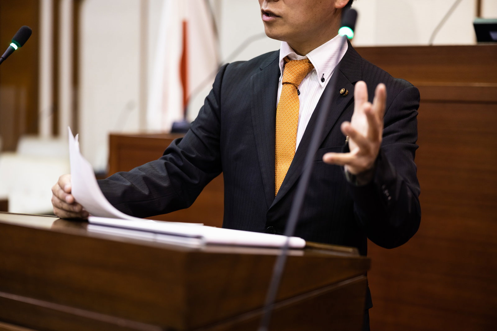 市議会の議場で身振り手振りで熱く主張する市議会議員の姿