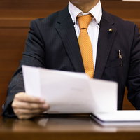 ネクタイのズレを気にせず原稿を持って熱弁する市議会議員の写真