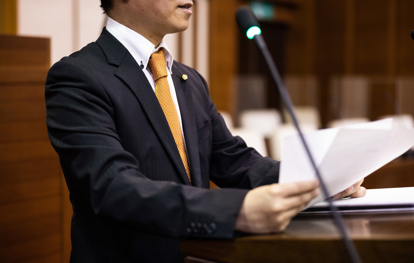 紙原稿を持ちながら市議会で発言する男性議員の議場での演説風景