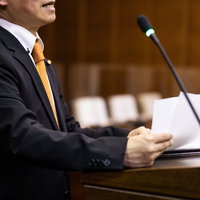 議員バッジをつけて市議会で熱弁する市議会議員の演説風景の写真