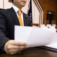 市議会の議場で原稿を手に登壇席で質問する議員の写真