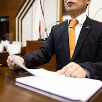 議長に見守られる中、議場で熱弁を振るう議員の写真