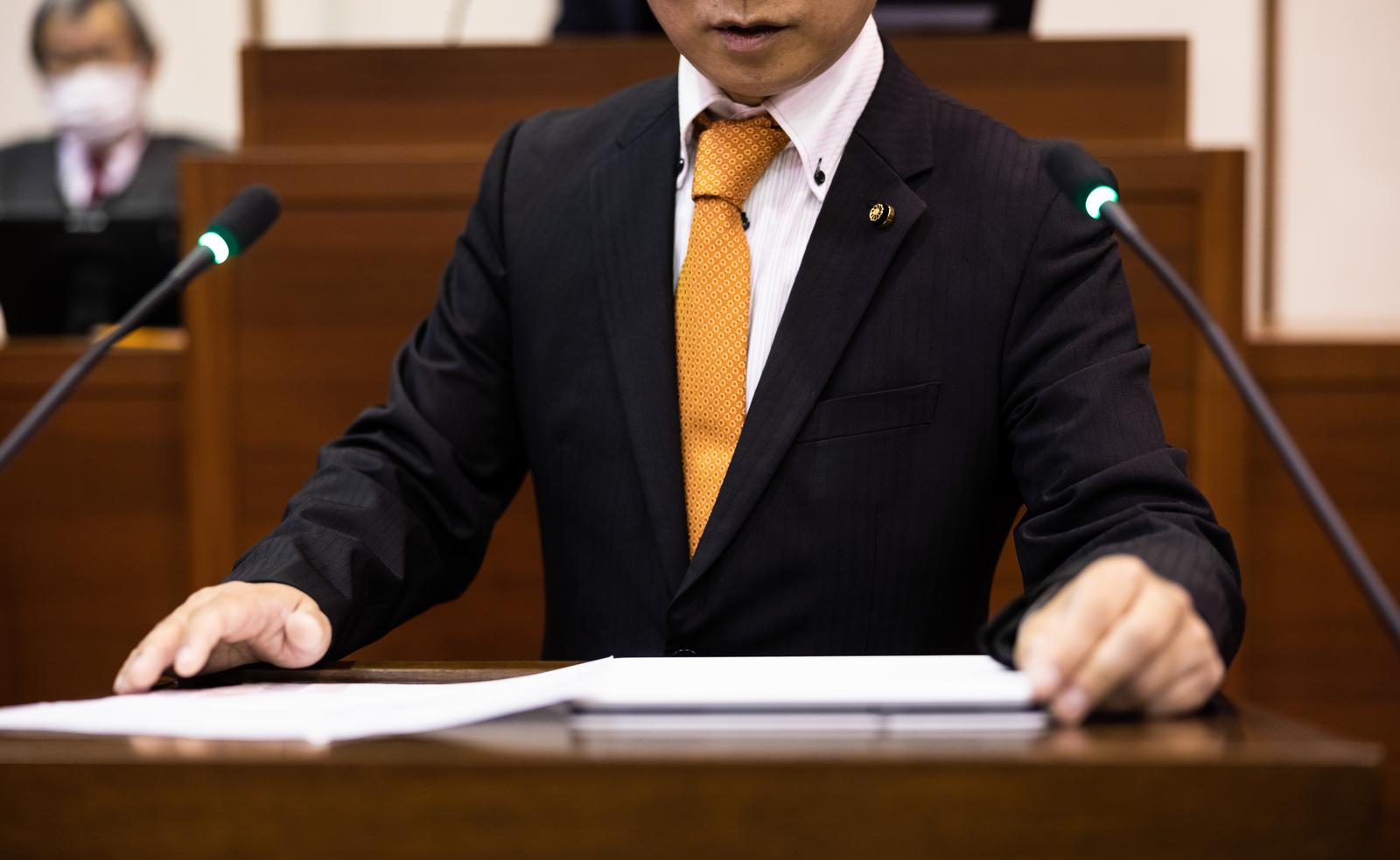 市議会の議場でマイクに向かって発言する男性議員