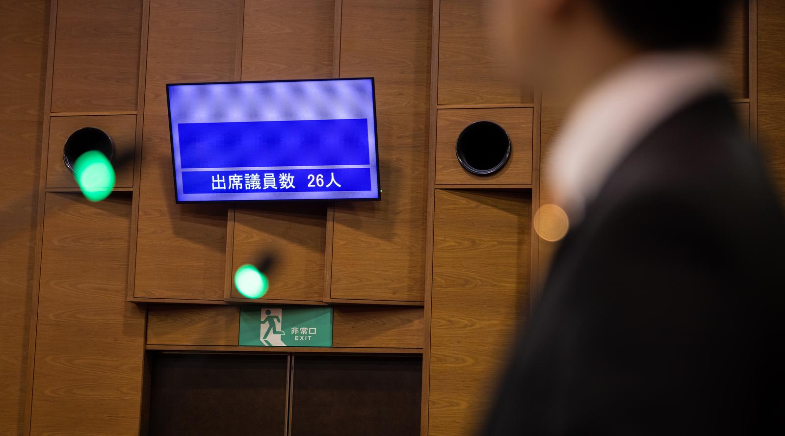 出席議員数26人を表示する電光板と緑色に点灯した信号機が設置された議会場の壁